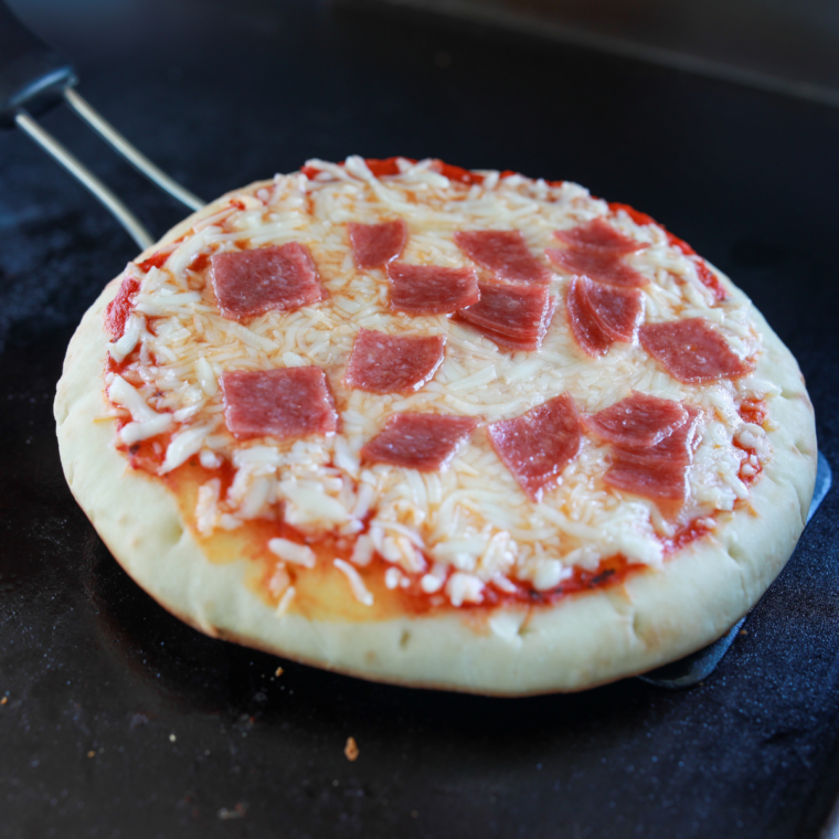 Lifting the crust with a spatula to check the golden bottom of Blackstone pizza
