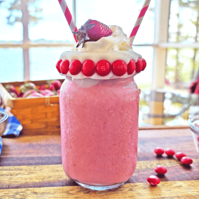 Glass of pink Skittles Strawberry Milkshake topped with whipped cream and rainbow candy pieces.