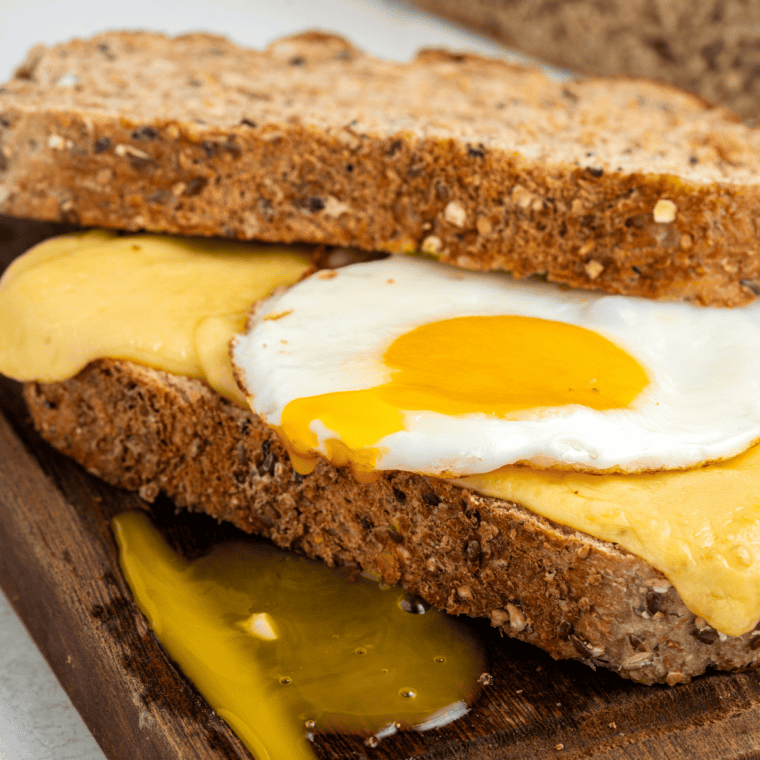 Air fryer sausage, bacon, and egg sandwich stacked with melted cheese on buttery toasted bread.