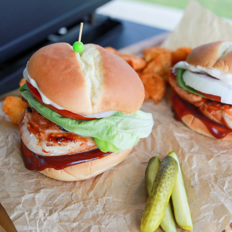 Blackstone BBQ chicken burger topped with crispy bacon, barbecue sauce, and melted cheese on a toasted bun.