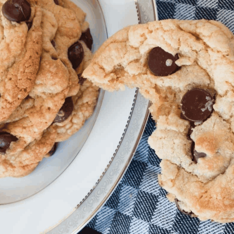 Freshly baked Copycat Otis Spunkmeyer Chocolate Chip Cookies stacked on a cooling rack with melty chocolate chips.