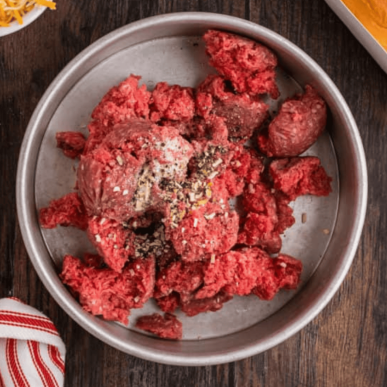 Seasoned ground beef being broken up with a spatula in a black air fryer basket preheated to 400°F.