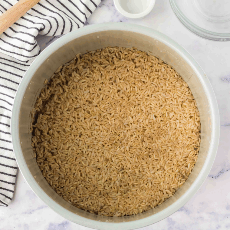 Toasted brown rice and butter mixed with onions and garlic in the Instant Pot, then cooking under high pressure with vegetable broth.