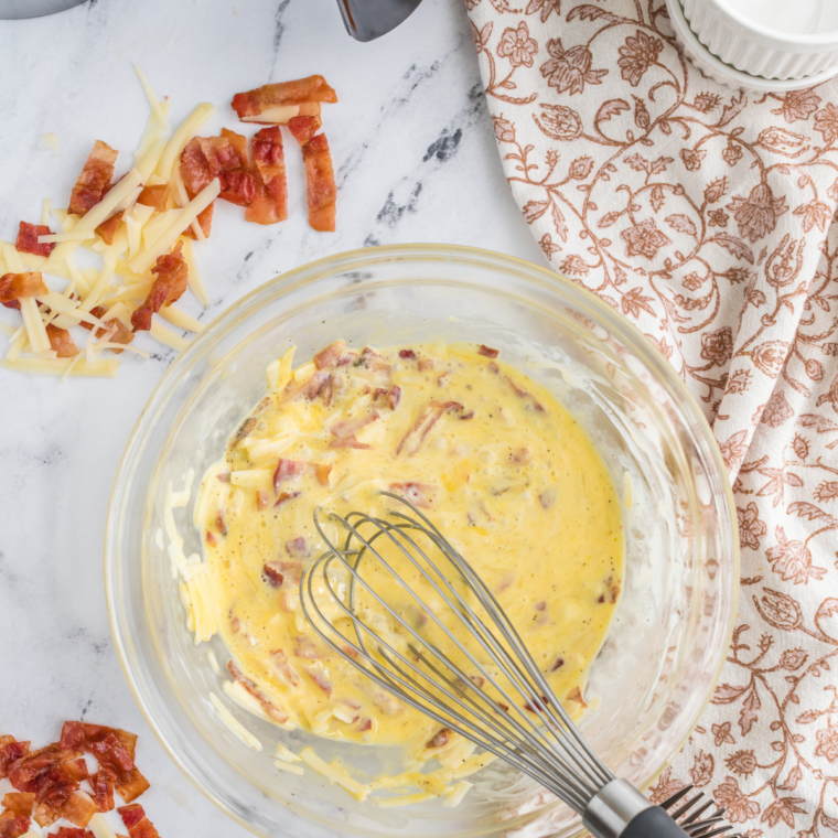 Whisked eggs and shredded cheese in a glass bowl for keto egg muffins