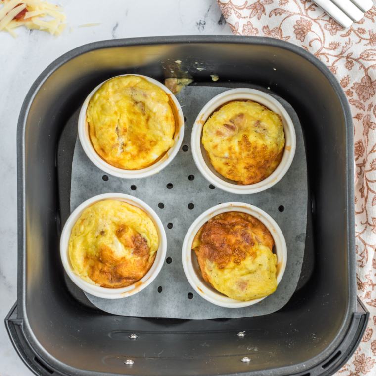 Cooked mini cheese frittatas puffed up in the muffin tin inside an air fryer