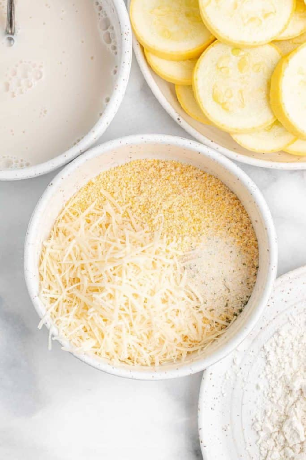 Three shallow bowls of flour, milk, and seasoned cornmeal set up for breading