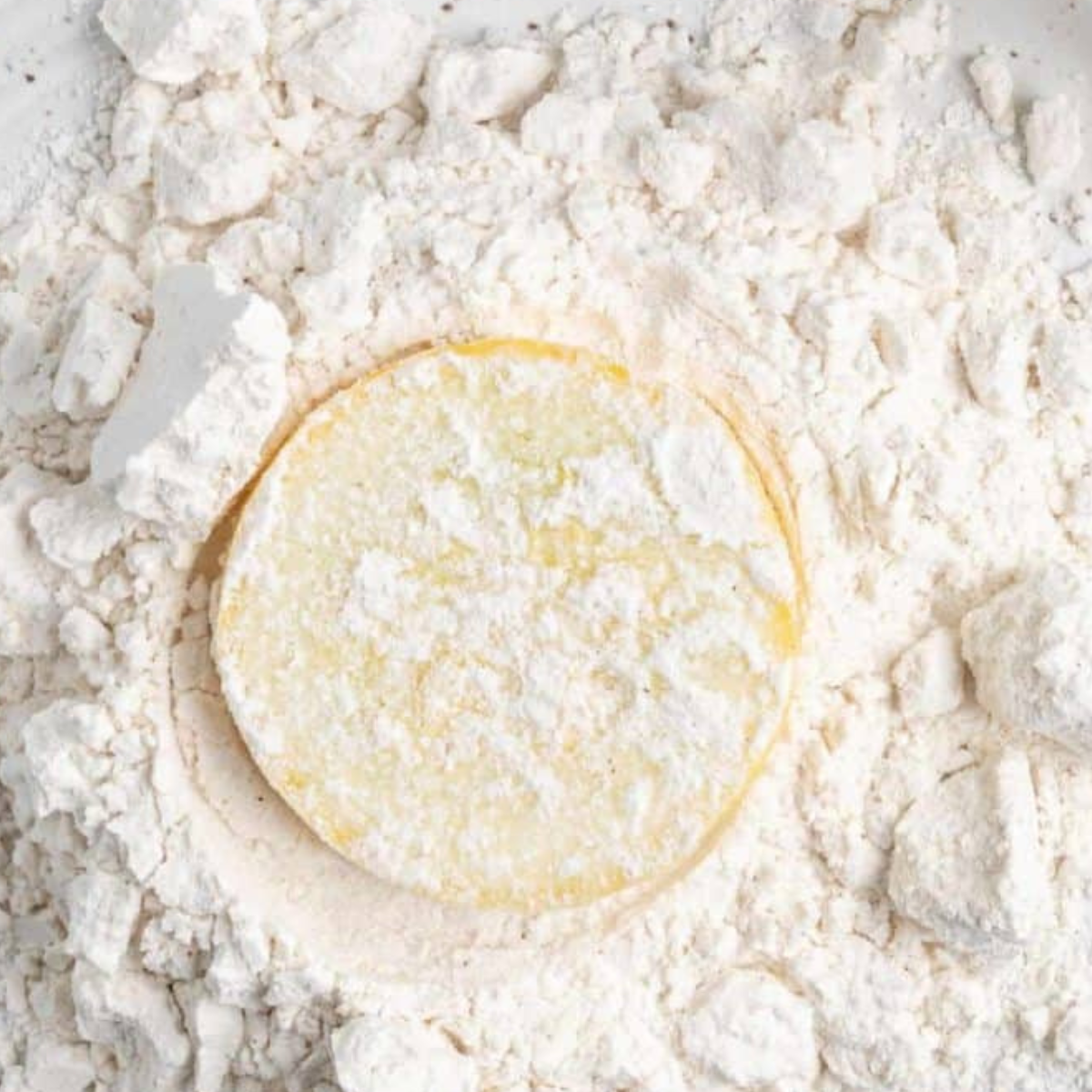 Yellow squash round being dipped into flour before the cornmeal coating