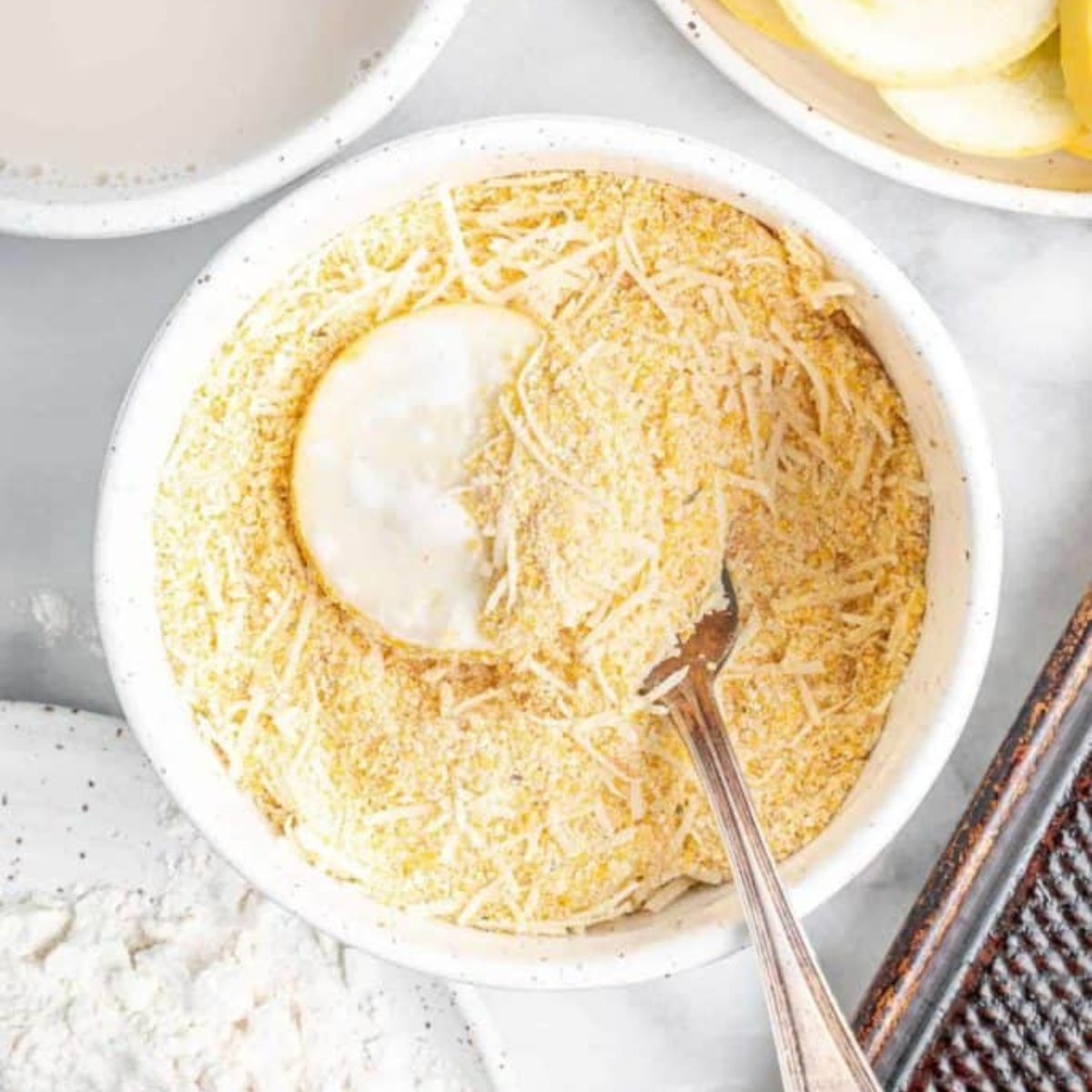 Yellow squash round being dipped into milk before the cornmeal coating