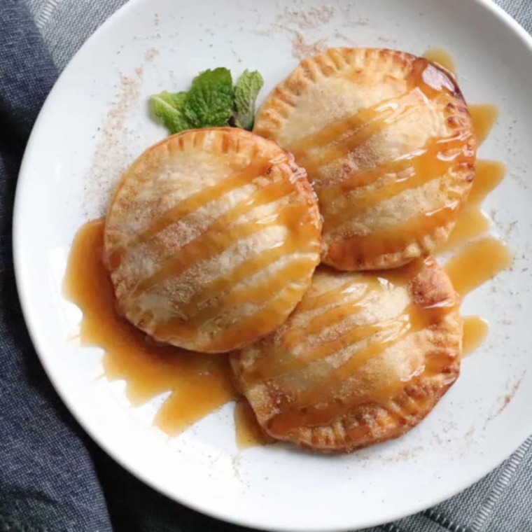 Finished air fryer caramel apple hand pies drizzled with caramel sauce and cinnamon sugar