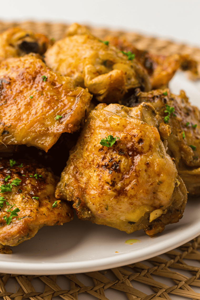 Golden-brown Ninja Crispi chicken thighs served on a plate with fresh herbs.