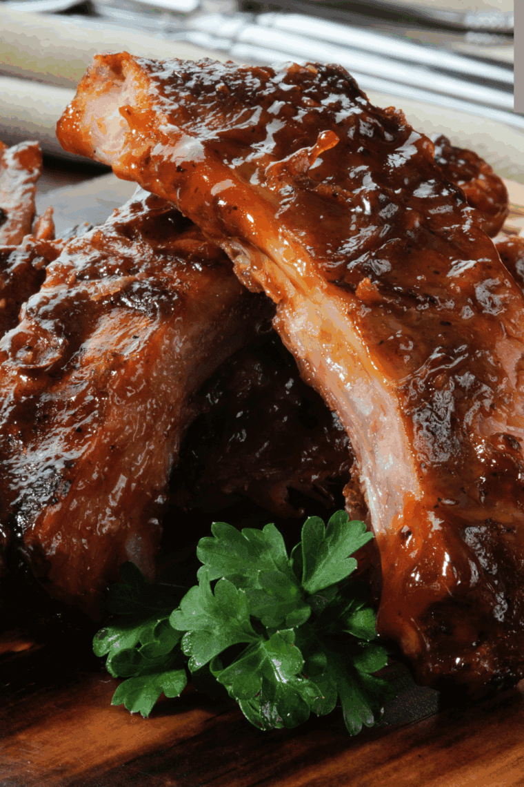 Tender 12 Bones Smokehouse Root Beer Baby Back Ribs coated in a sticky glaze, garnished with fresh herbs, served on a platter.