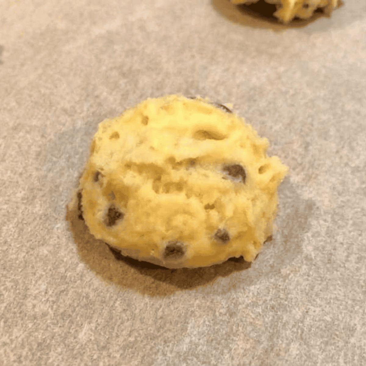Scooping blueberry muffin batter onto parchment paper in an air fryer basket, ready to cook.