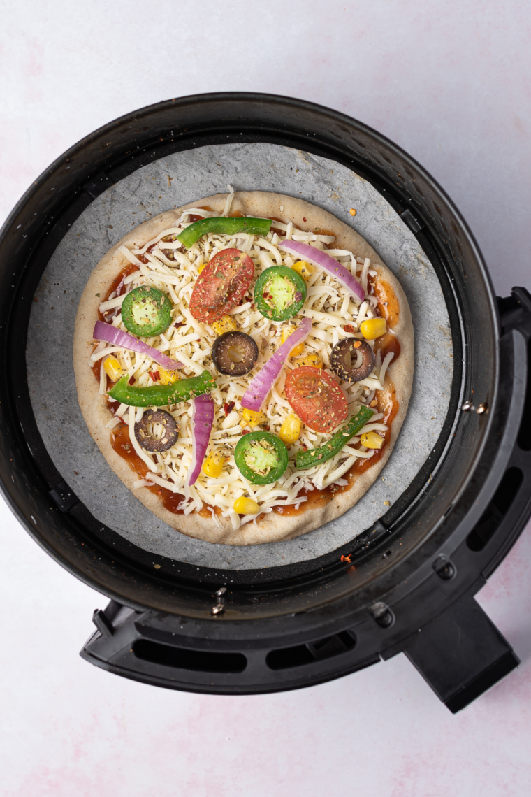 Pita pizza cooking in an air fryer at 360°F with bubbling melted mozzarella cheese and crisp golden edges