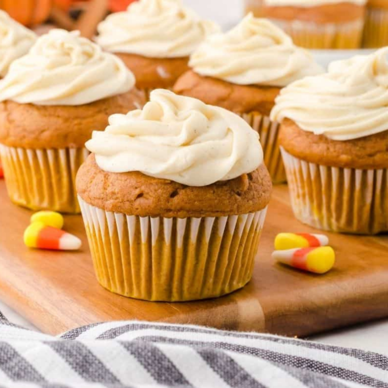 Piping cream cheese frosting onto a cooled pumpkin spice cupcake