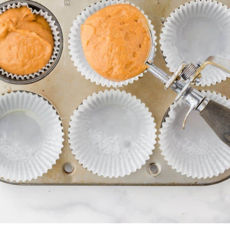 Cupcake liners filled two-thirds full with pumpkin spice batter in a muffin tin