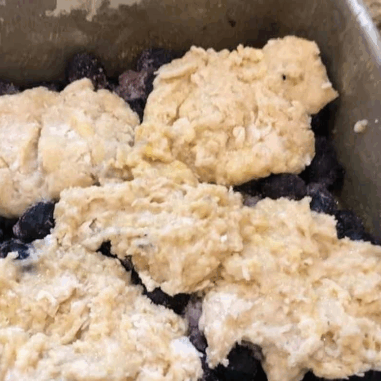 Spooning cobbler batter over the blueberry filling in a greased air-fryer-safe baking dish before cooking