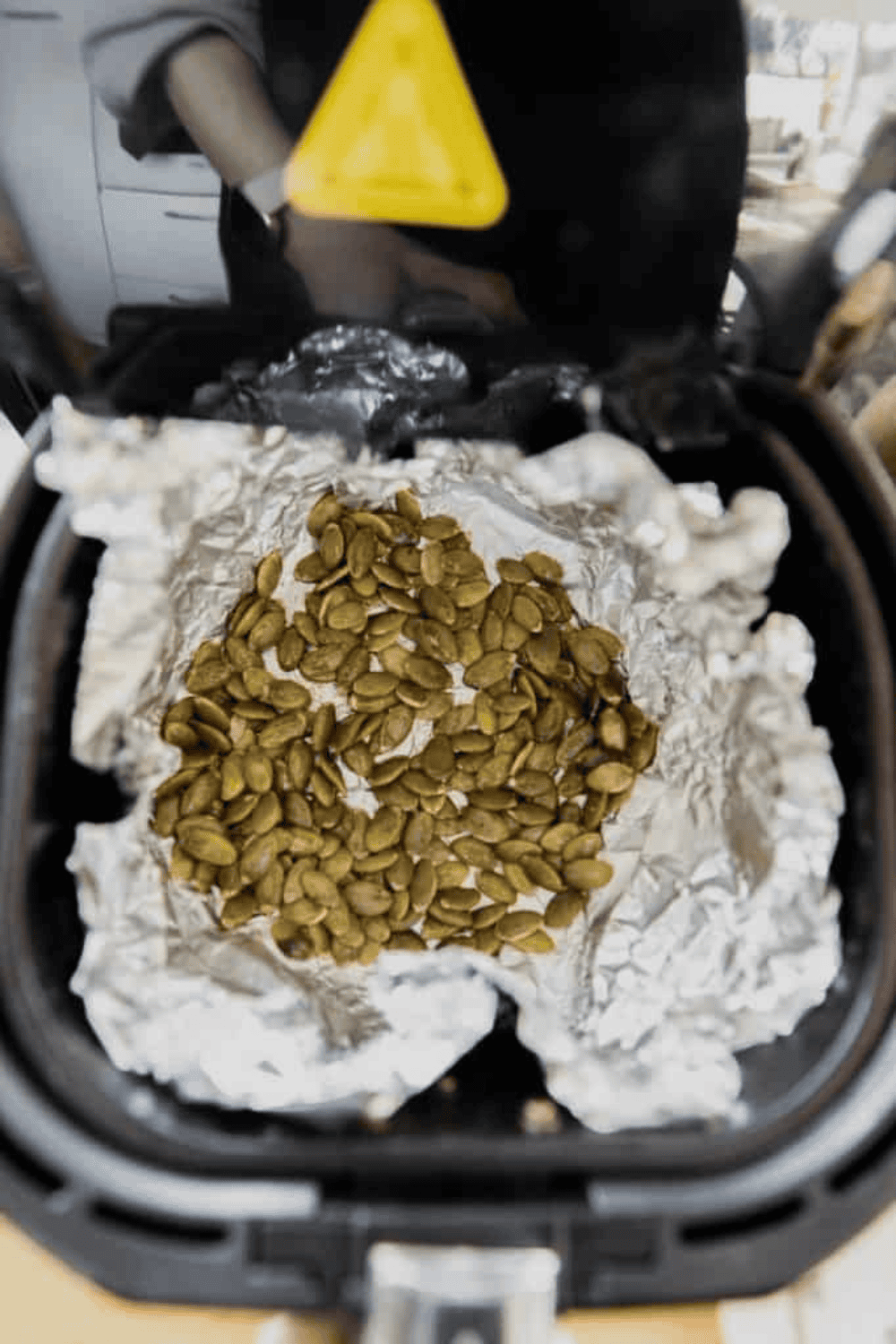 Pepitas spread in a single layer in the air fryer basket, cooking until golden, with shaking for even roasting.