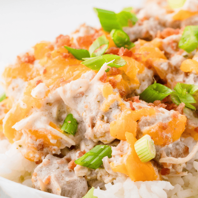 Creamy Instant Pot crack chicken topped with crispy bacon and sliced green onions in a white bowl