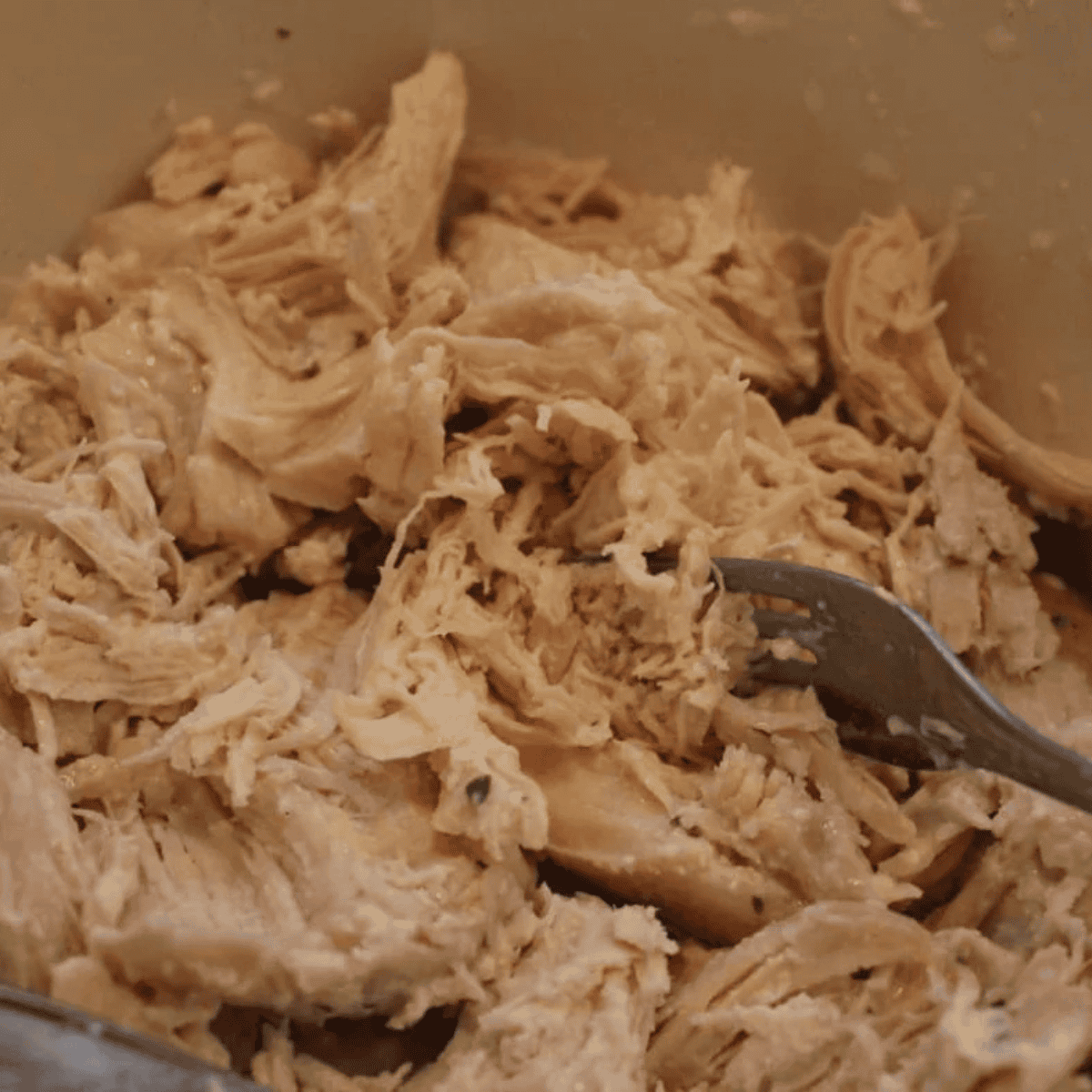 Shredding cooked chicken with two forks in a mixing bowl