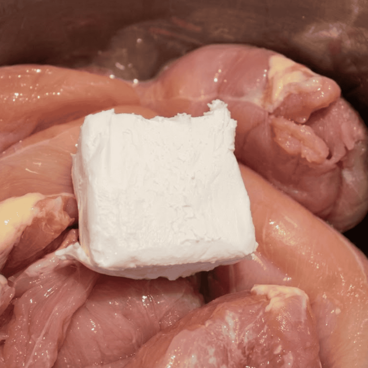 Raw chicken breasts in an Instant Pot with a block of cream cheese on top