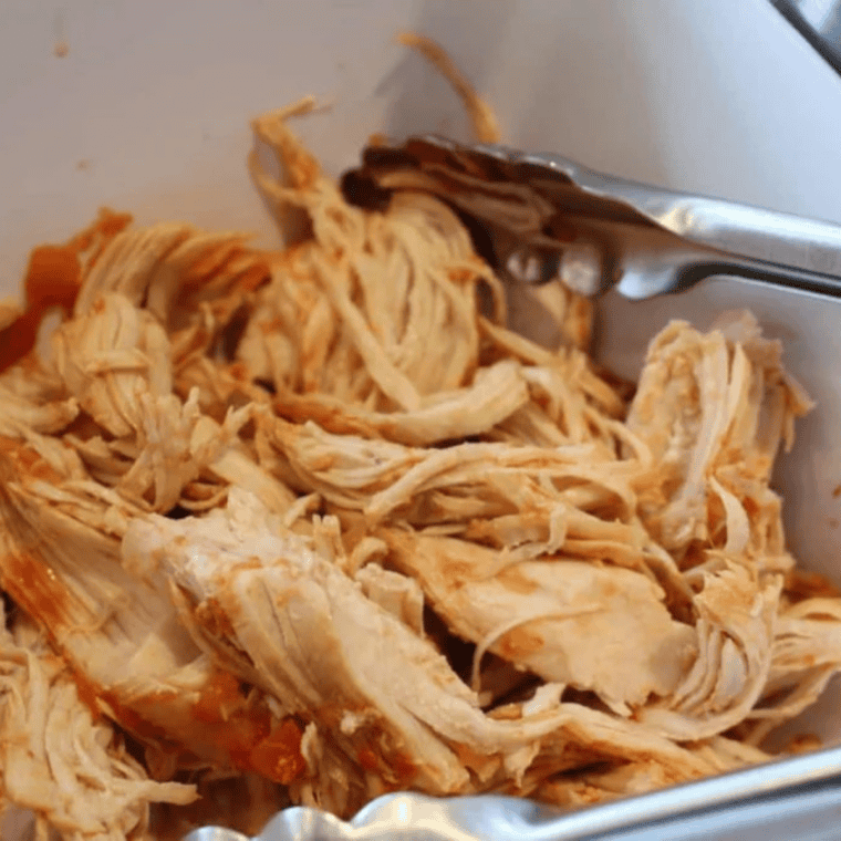 Cooked salsa chicken being shredded with two forks right in the Instant Pot