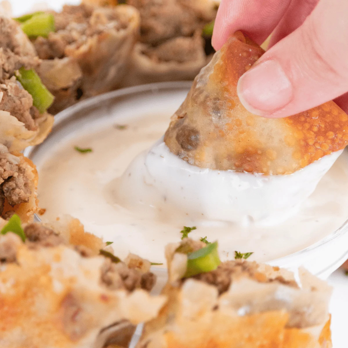 Cheesesteak egg rolls sliced on the diagonal and standing upright on a plate beside horseradish sauce