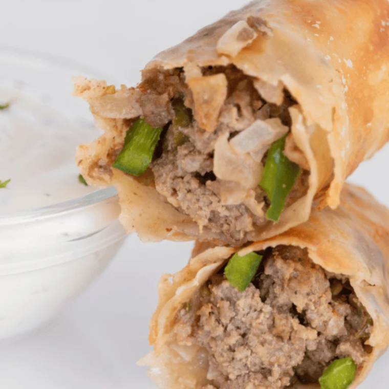 Close up of a cheesesteak egg roll broken open with melted provolone, shaved steak, peppers, and onions inside