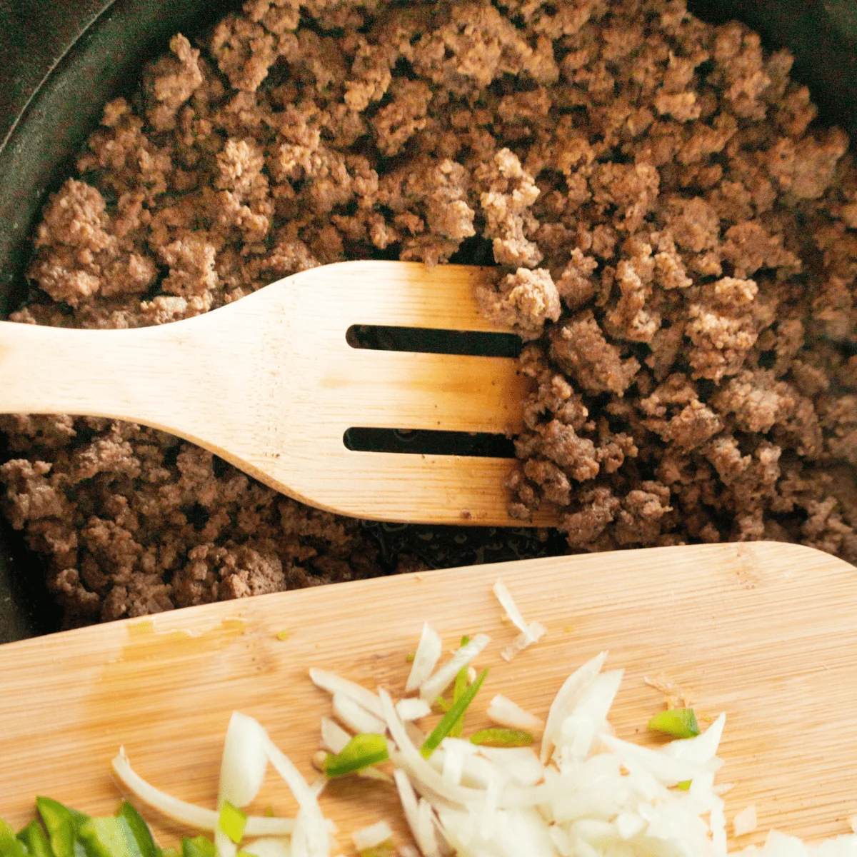 Shaved steak searing in a hot skillet, browned and broken apart with a spatula