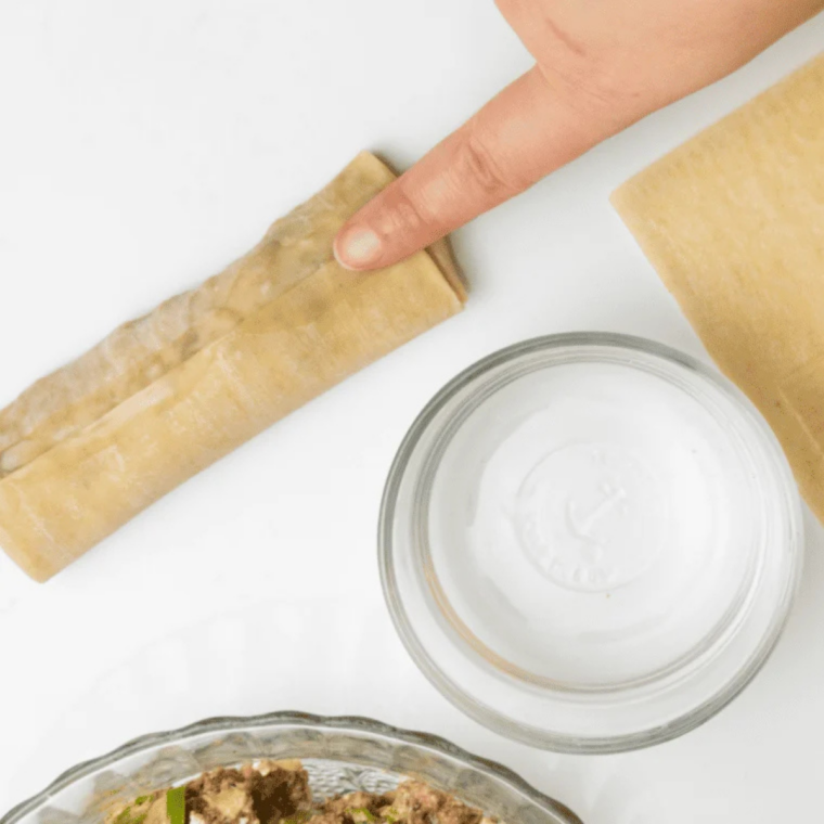 Egg roll wrapper in a diamond shape with cheesesteak filling in the center, corners folded in before rolling