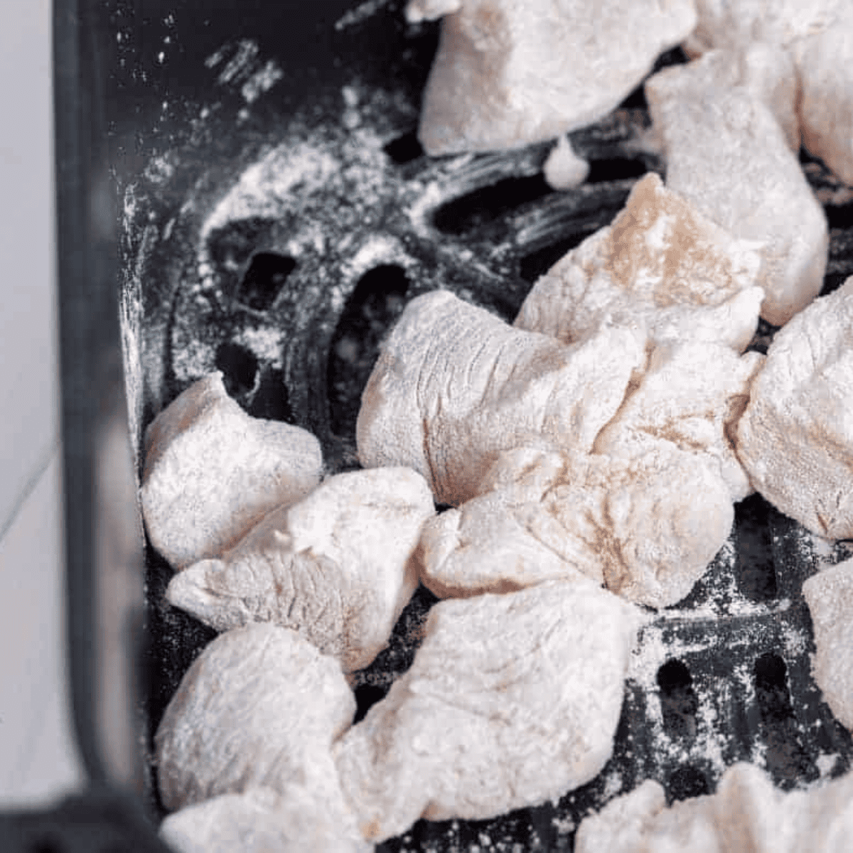 Diced chicken pieces being coated evenly with potato starch in a large mixing bowl.