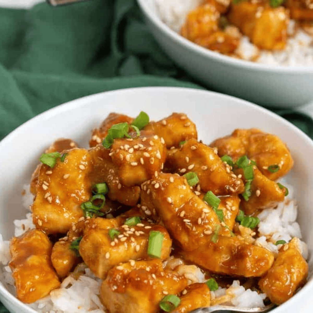 Crispy sesame chicken coated in glossy sauce, topped with sesame seeds and green onions on a plate.