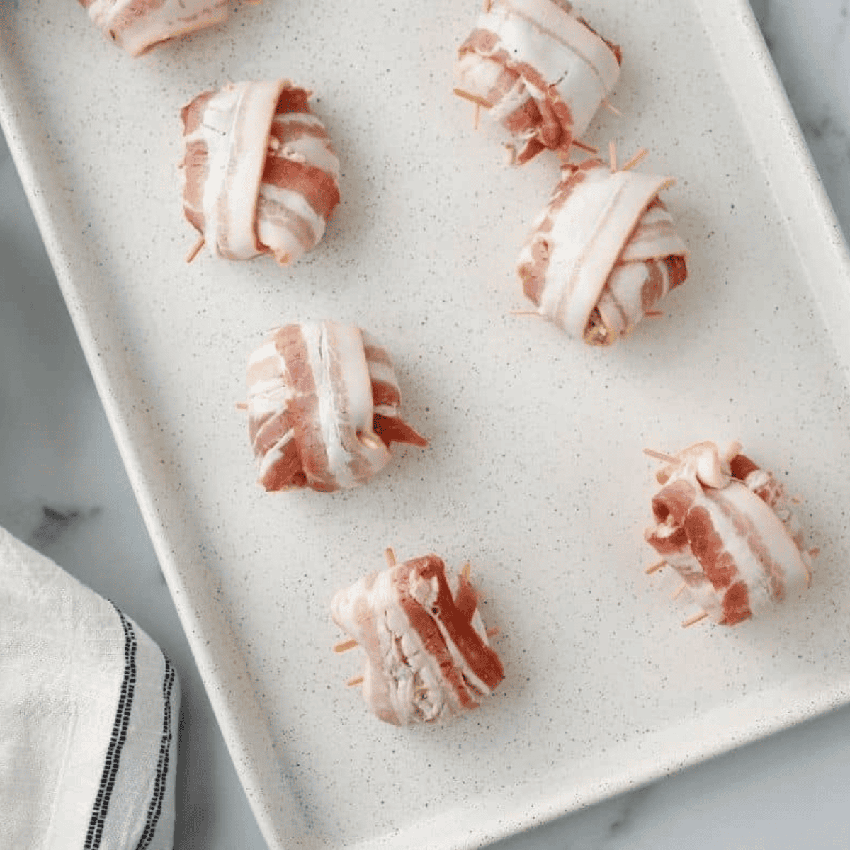 Bacon-wrapped crab rolls shaped and secured with toothpicks ready for air frying.