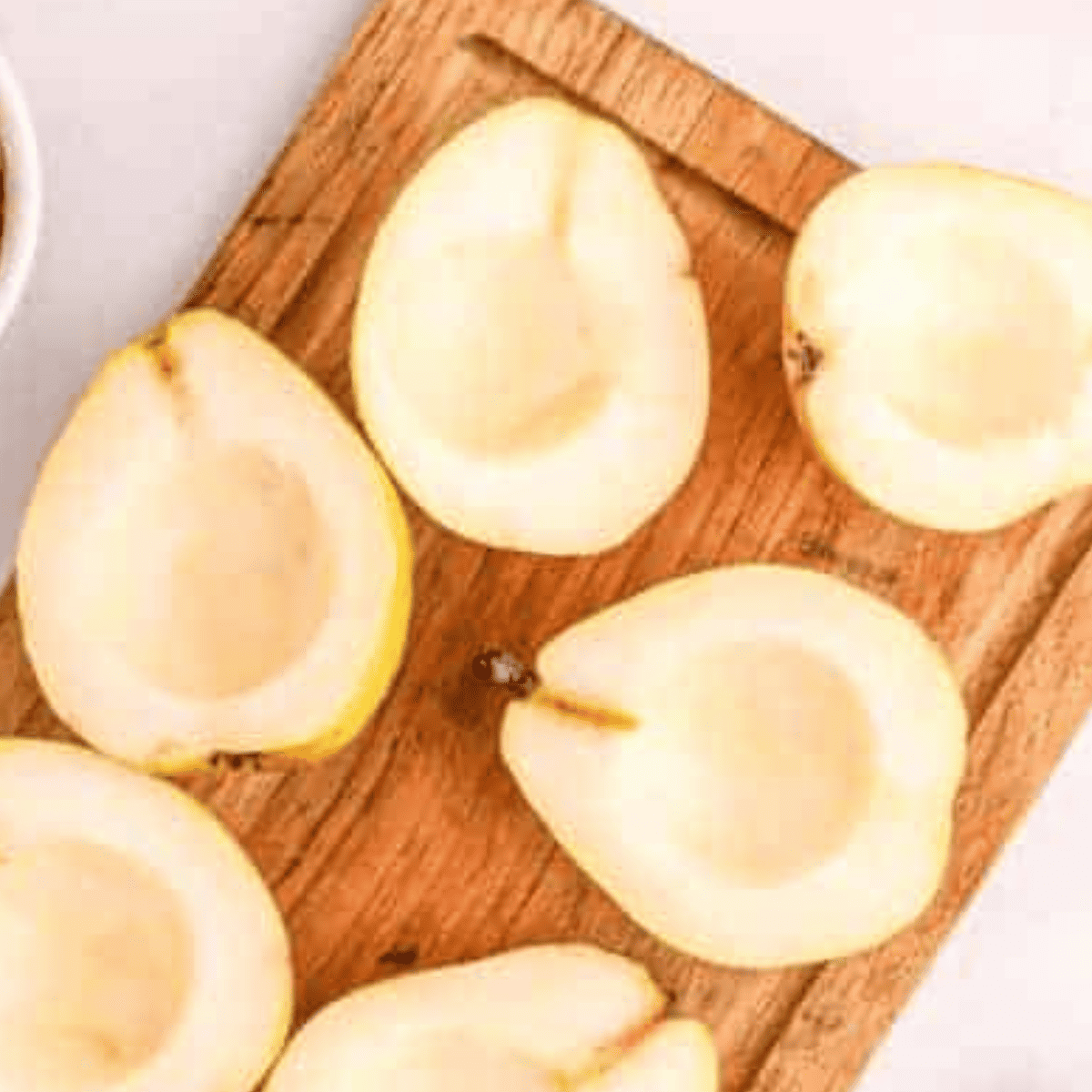 Halved fresh pears with cores removed next to a small bowl of cinnamon and sugar mixture for air fryer baked pears.