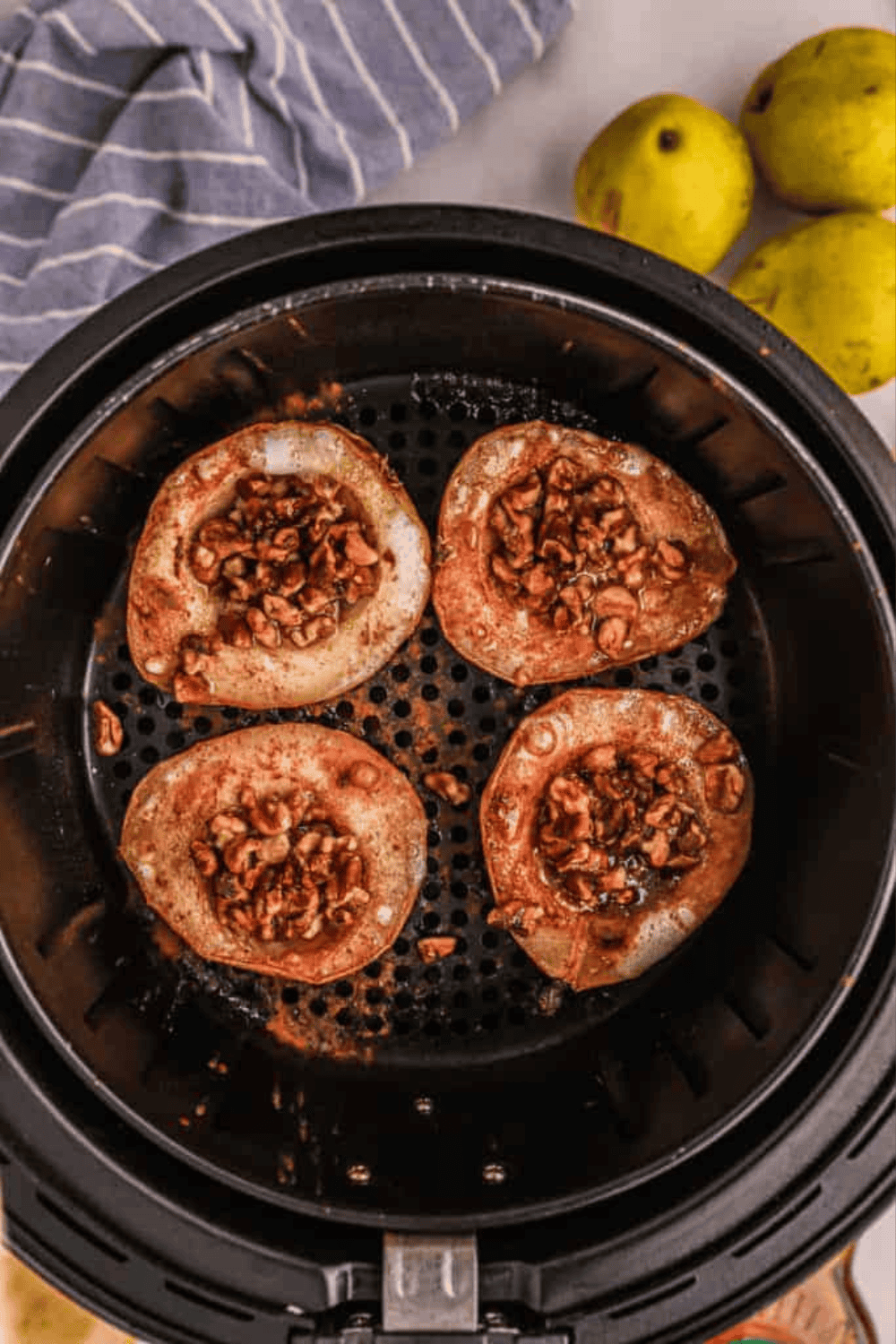 Pear halves filled with butter and topped with cinnamon sugar and chopped nuts before air frying.