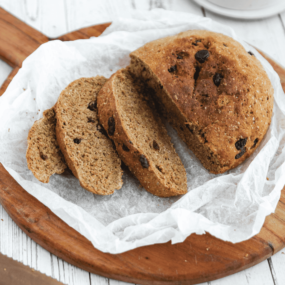 Air fryer Boston brown bread loaf sliced on a wooden board, showing the dense molasses-and-raisin crumb