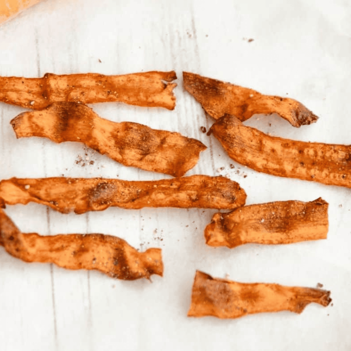 Crispy air fryer carrot bacon strips stacked on a white plate