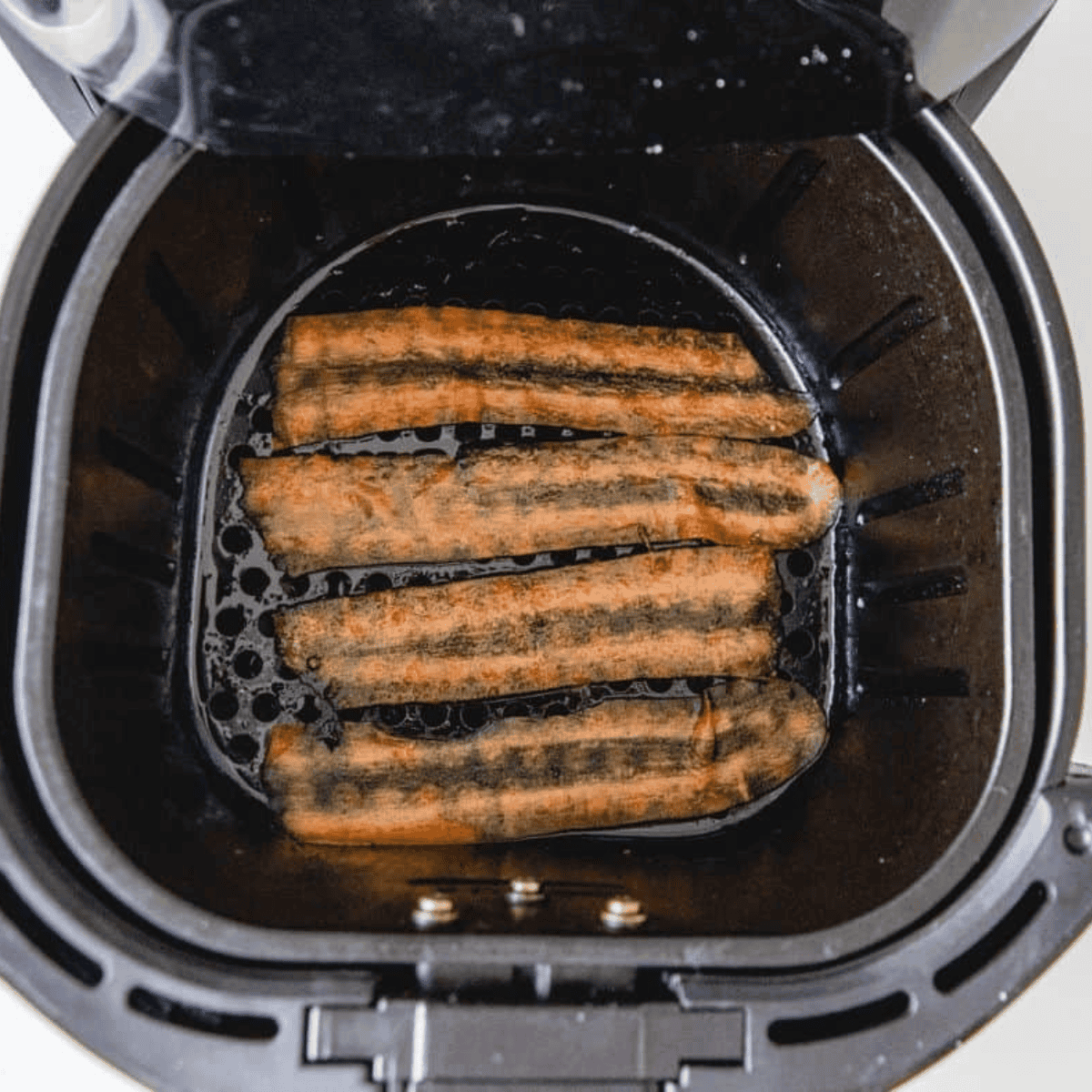 Carrot bacon strips in a single layer inside the air fryer basket