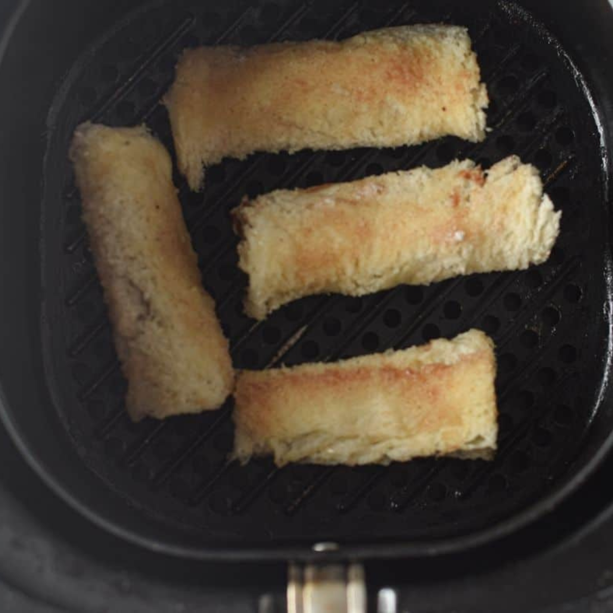 Bread rolls coated in egg and cinnamon sugar placed in air fryer basket, brushed with butter, cooking to golden brown