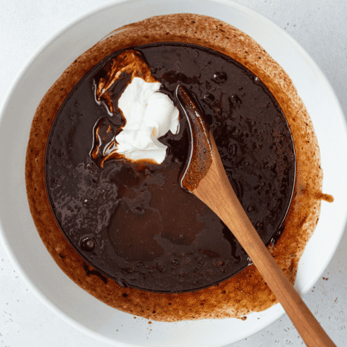 Melted dark chocolate and butter being stirred together until smooth and glossy.
