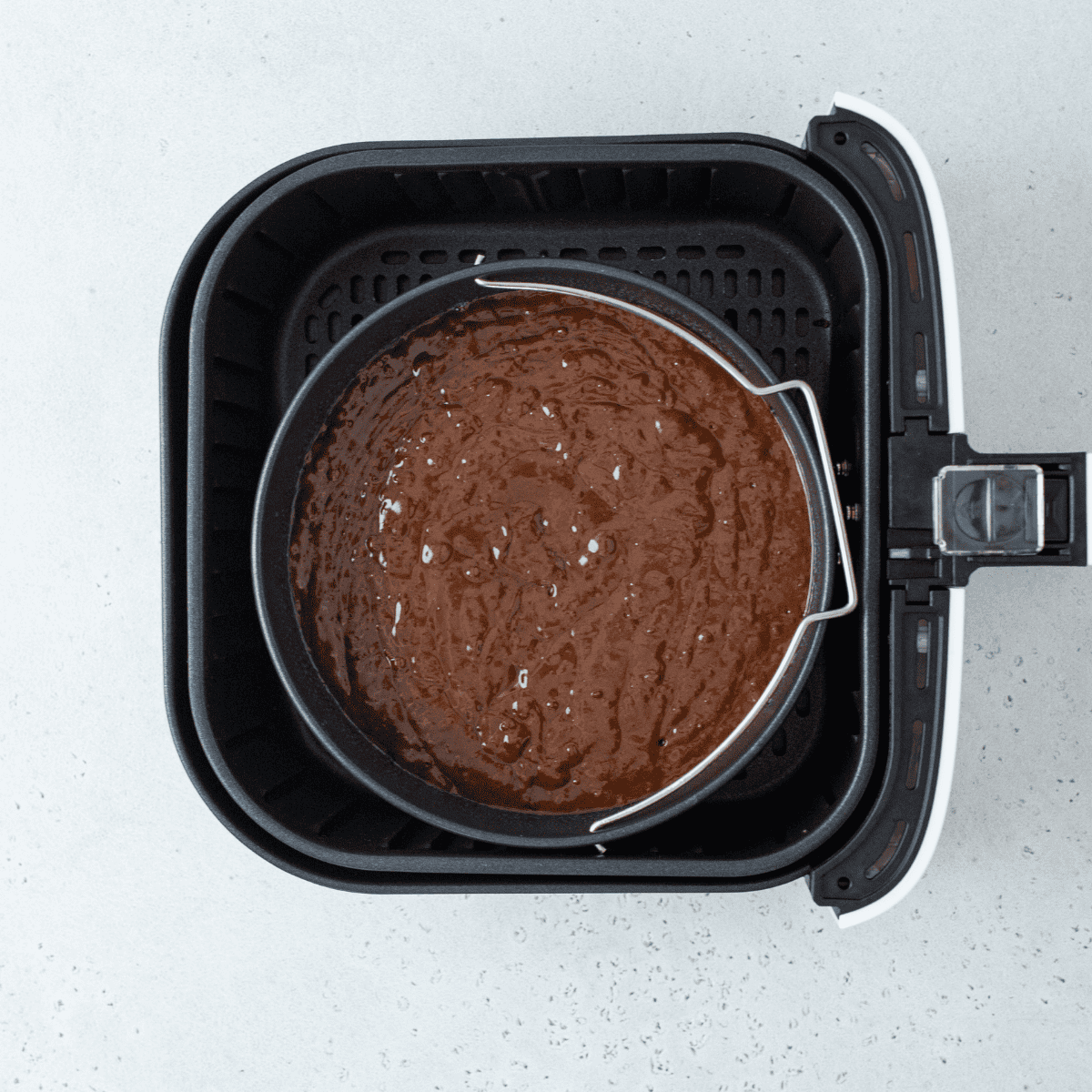 Flourless chocolate cake baking inside an air fryer basket until the edges are set.