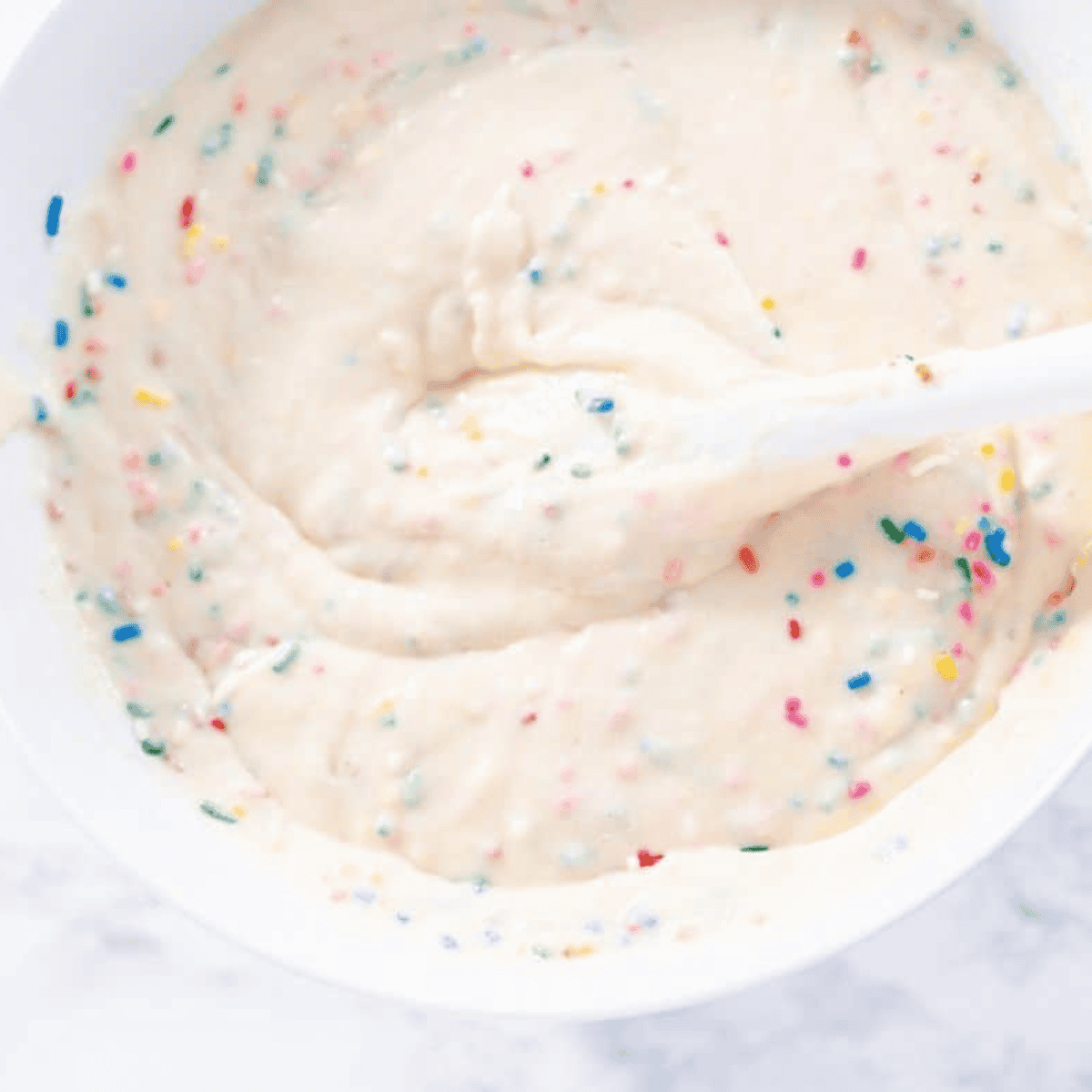 Wet ingredients including butter, egg whites, vanilla, sour cream, and milk combined with sprinkles in a separate bowl