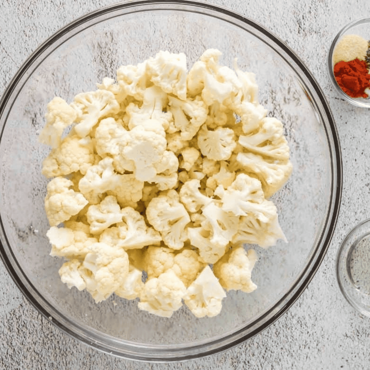 Seasoned cauliflower florets being loaded into the air fryer basket for roasting.