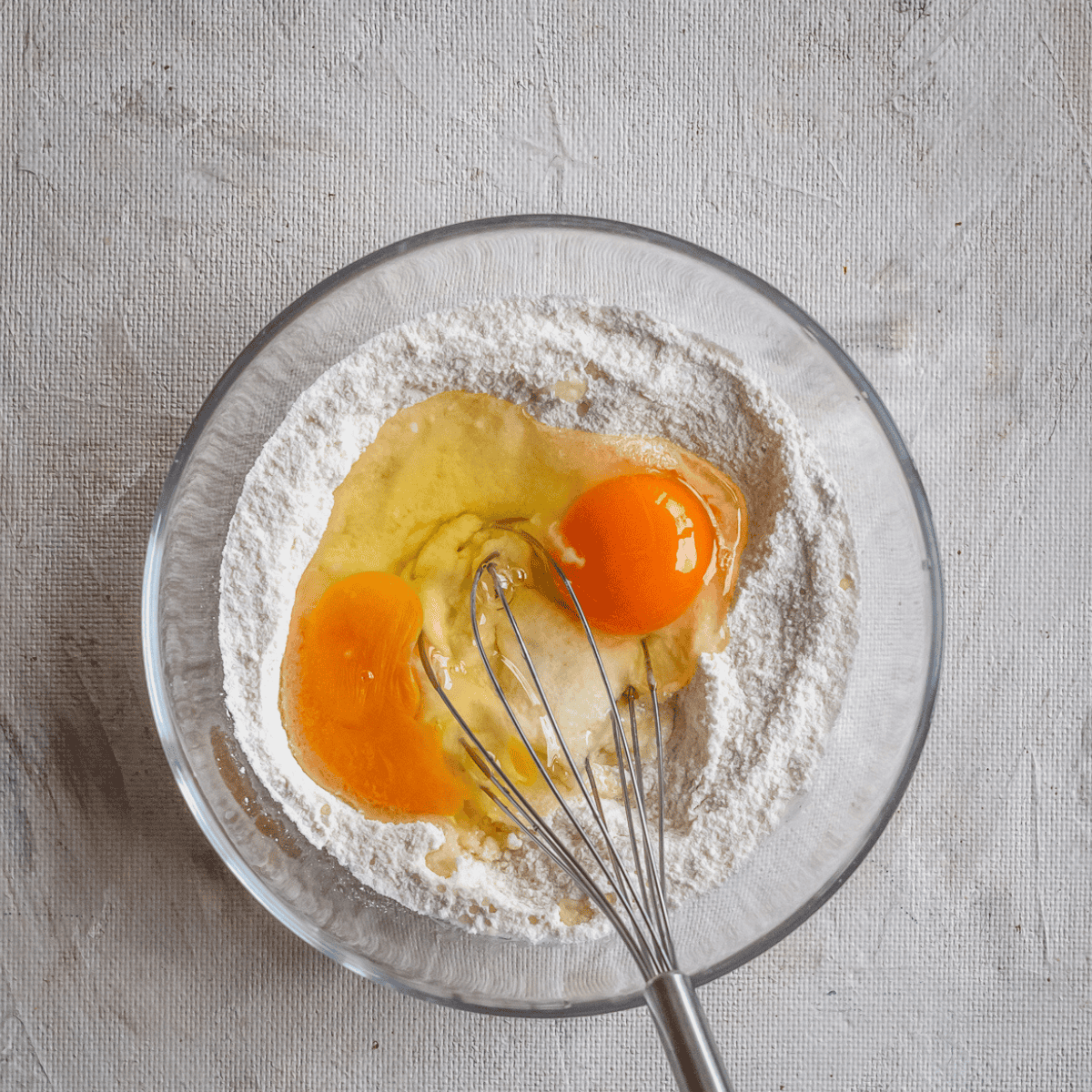 Mixing walnut cake batter with flour, sugar, eggs, vanilla, oil, and milk in a bowl after preparing a parchment-lined 7-inch baking pan.