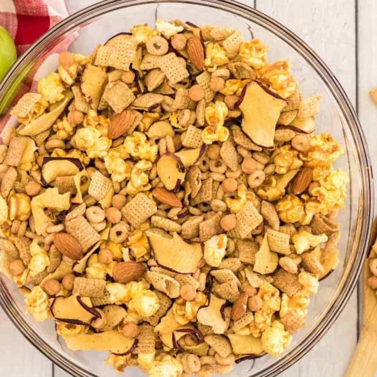 Melted butter being poured over cinnamon Chex, Cheerios, apple chips, and almonds in a large mixing bowl