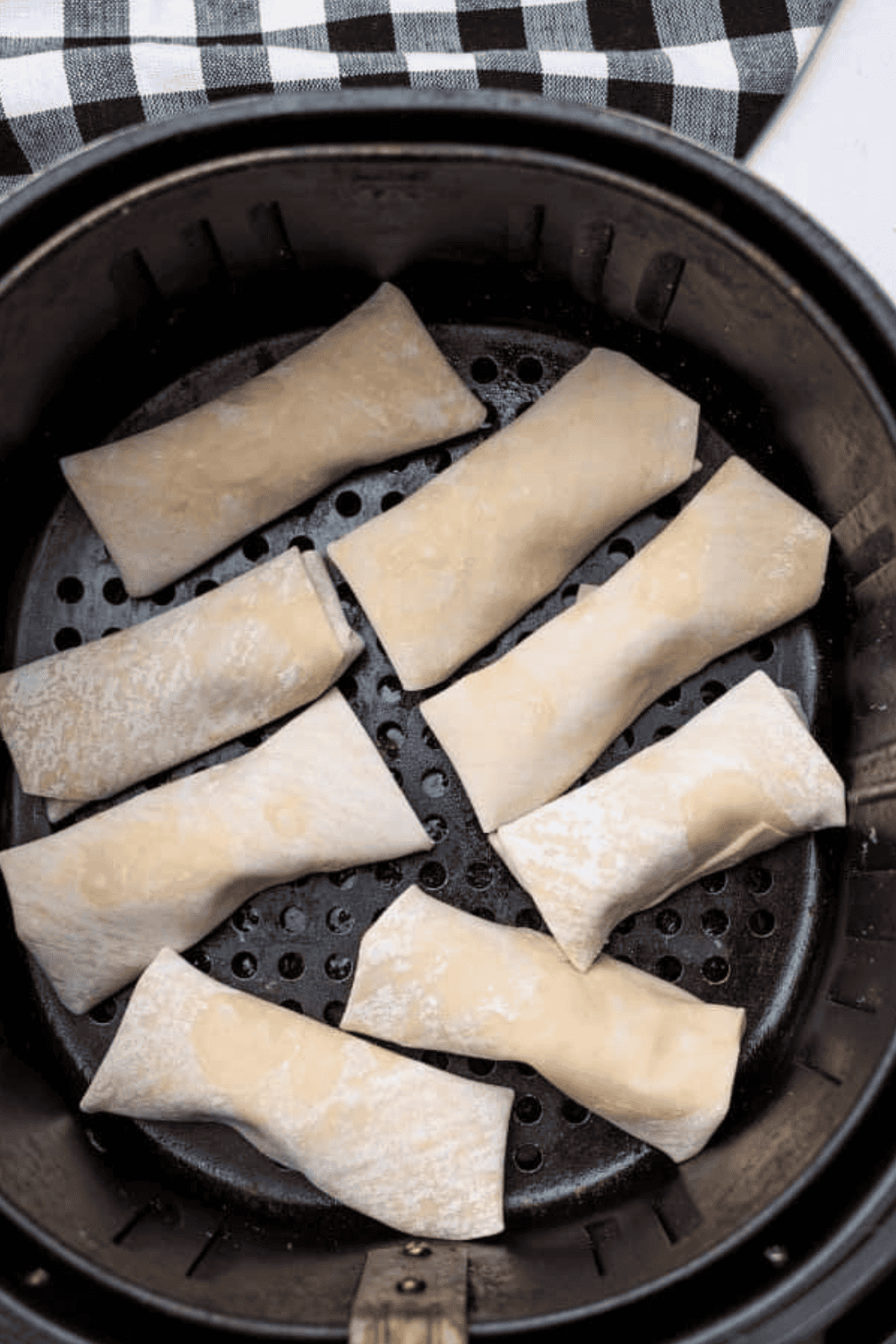 Egg rolls arranged in air fryer basket cooking to golden brown and crispy