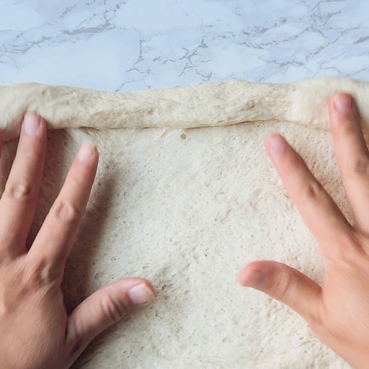Pizza dough rolled out on a floured surface into a thin rectangle.