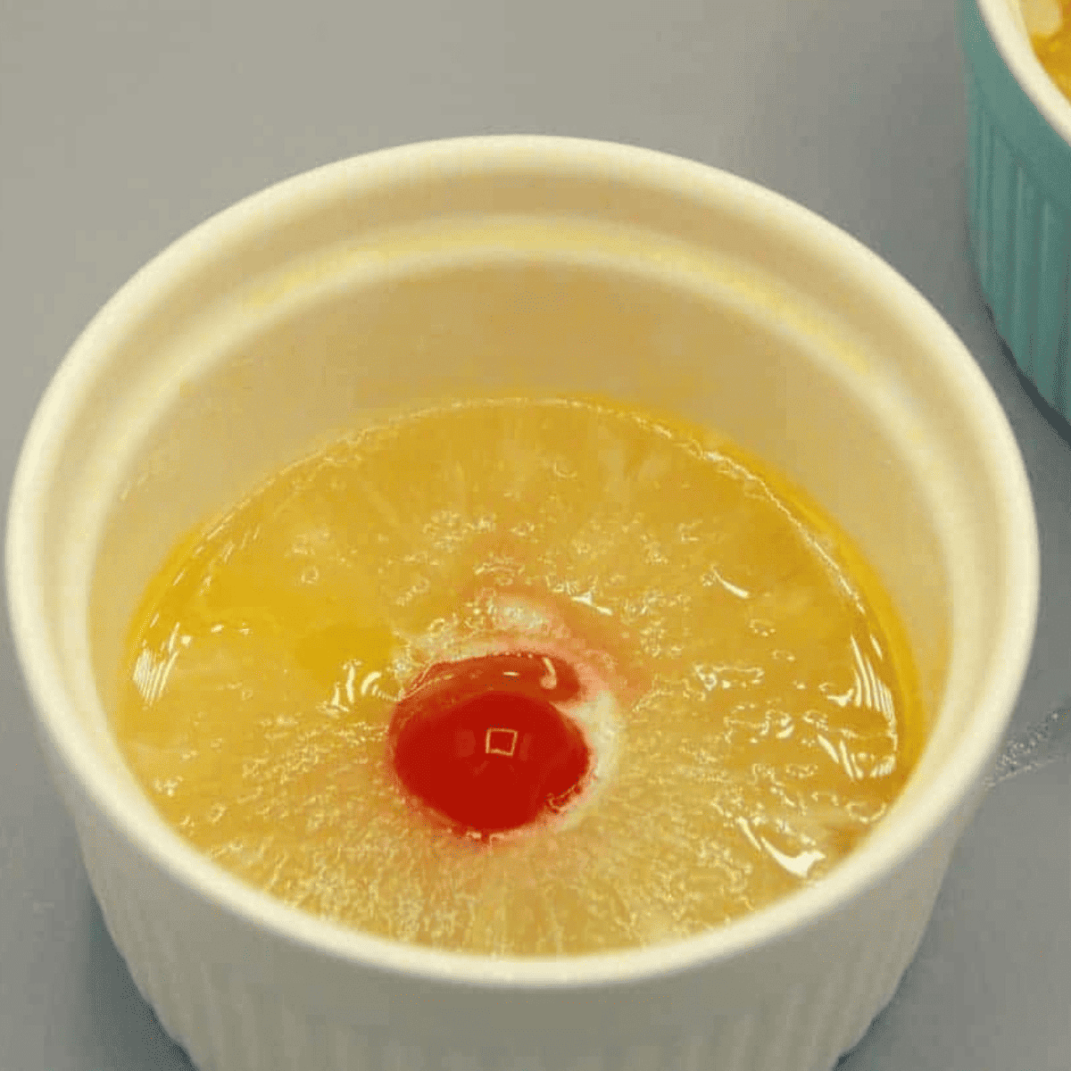 Ramekin prepared with butter, brown sugar, pineapple slice, and cherry on top.