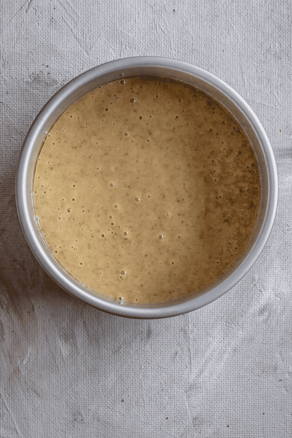 Walnut cake batter in a small baking pan placed in an air fryer basket, ready to bake until golden and fully cooked.