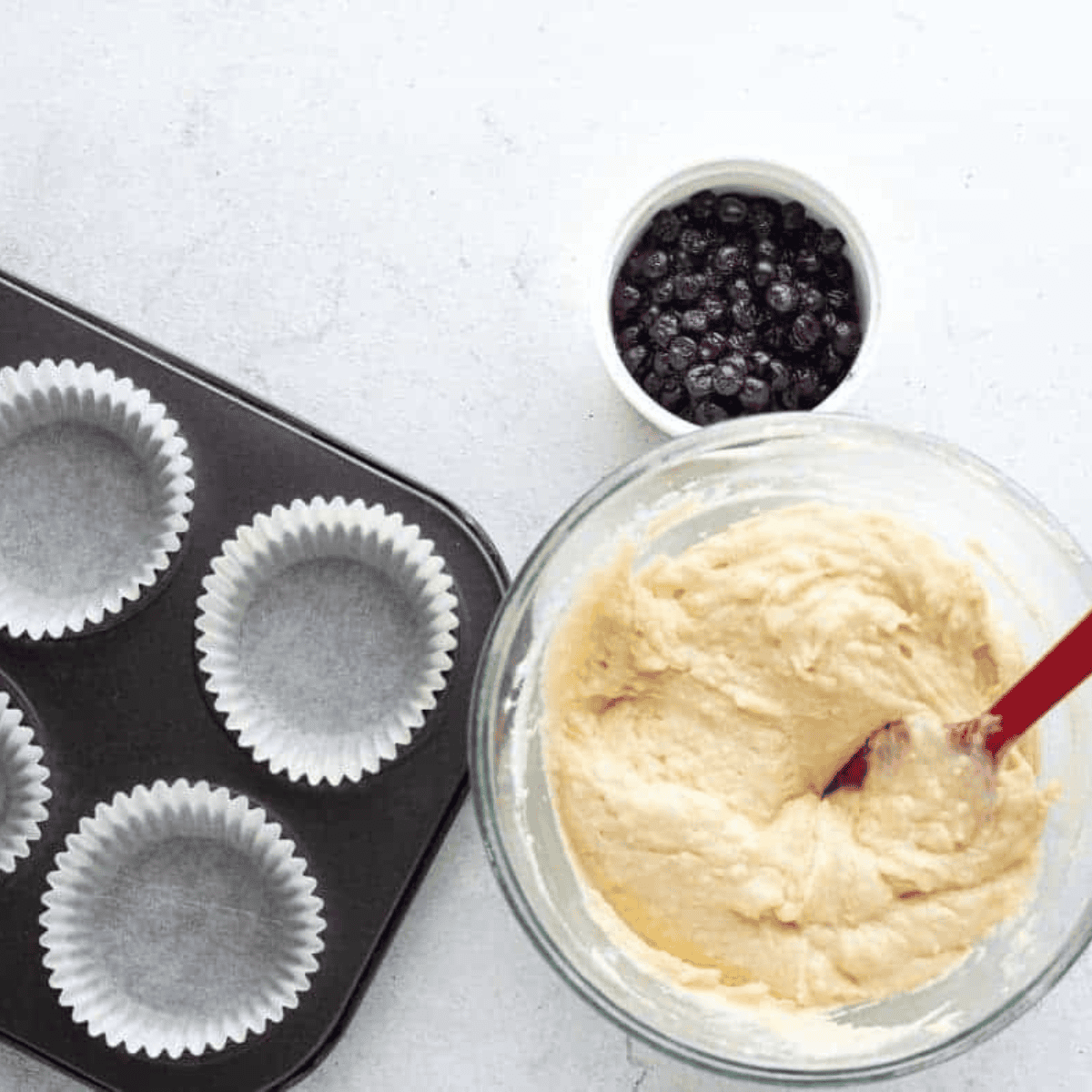 Mixing butter and sugar until creamy, then adding eggs, vanilla, flour, milk, and blueberries to form cupcake batter.