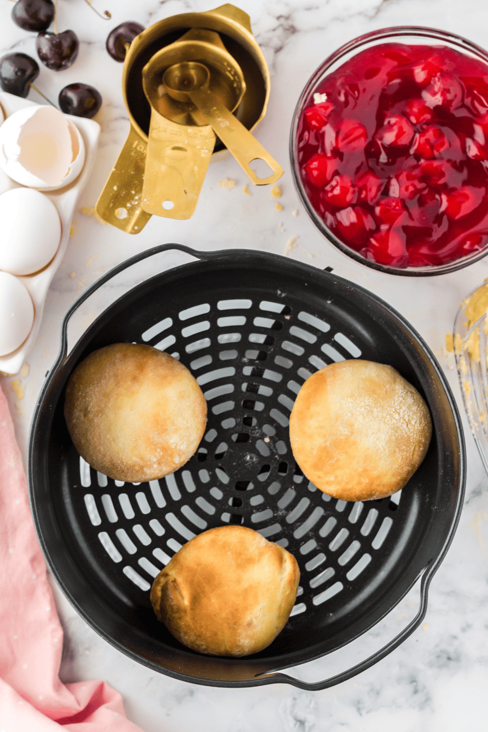 Placing sealed cherry pie donuts in the air fryer basket.